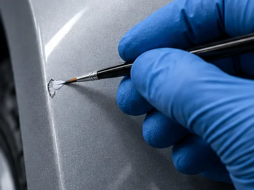 Gloved hand touching up a paint chip on a silver fender at Glenbard Auto Body in Lombard, IL